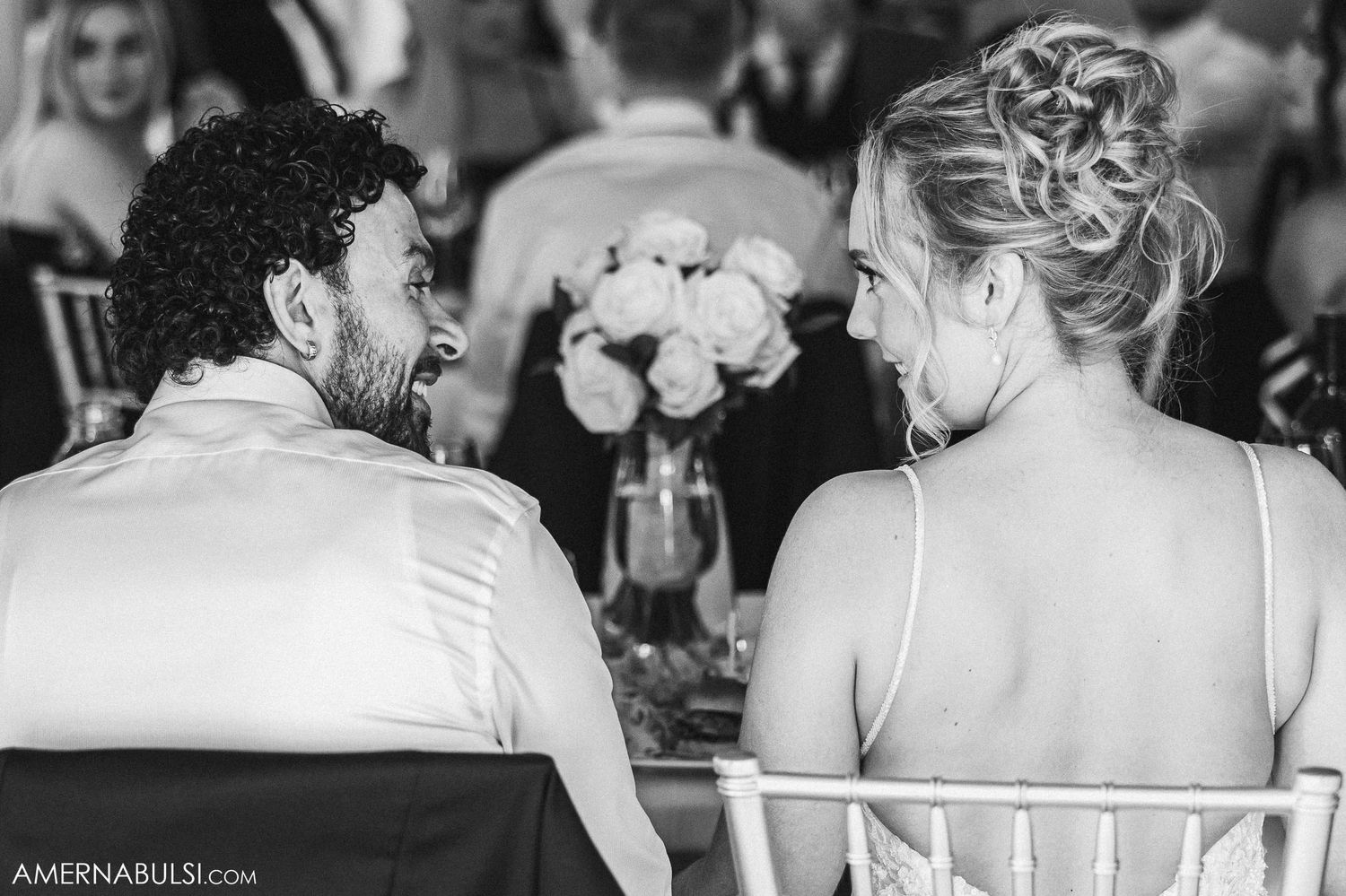 Black and white candid reception photo of newlyweds seated at dining table.