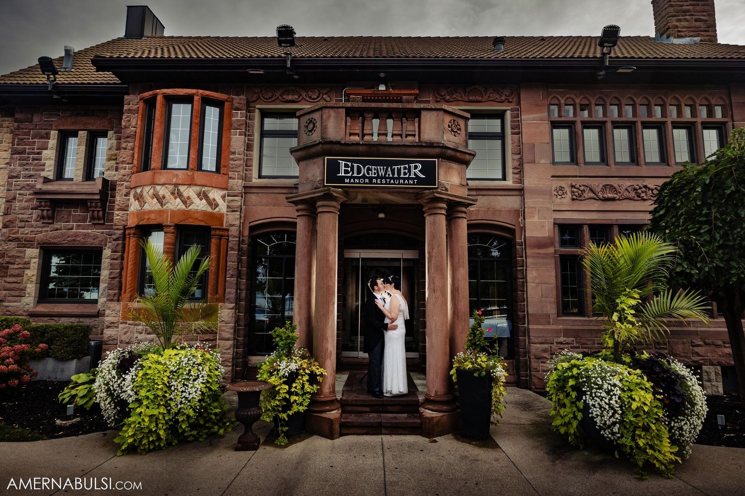 A couple stands in front of a brick Brunswick restaurant entrance adorned with lush greenery and potted palms.