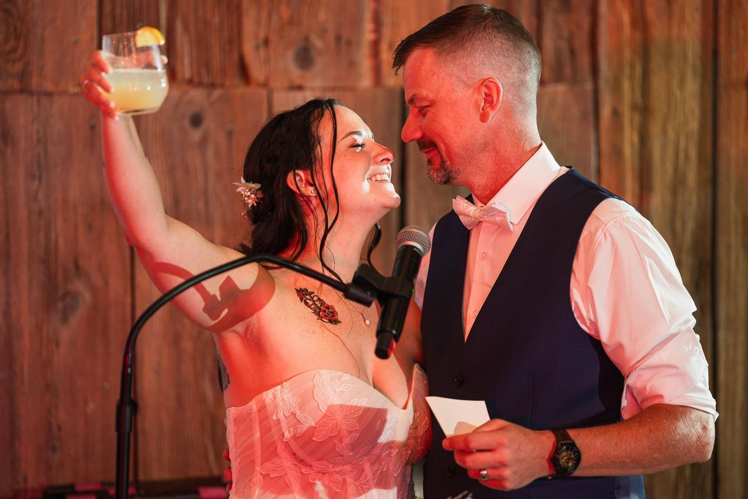 A celebratory moment at wedding reception with drink raised in rustic venue setting.