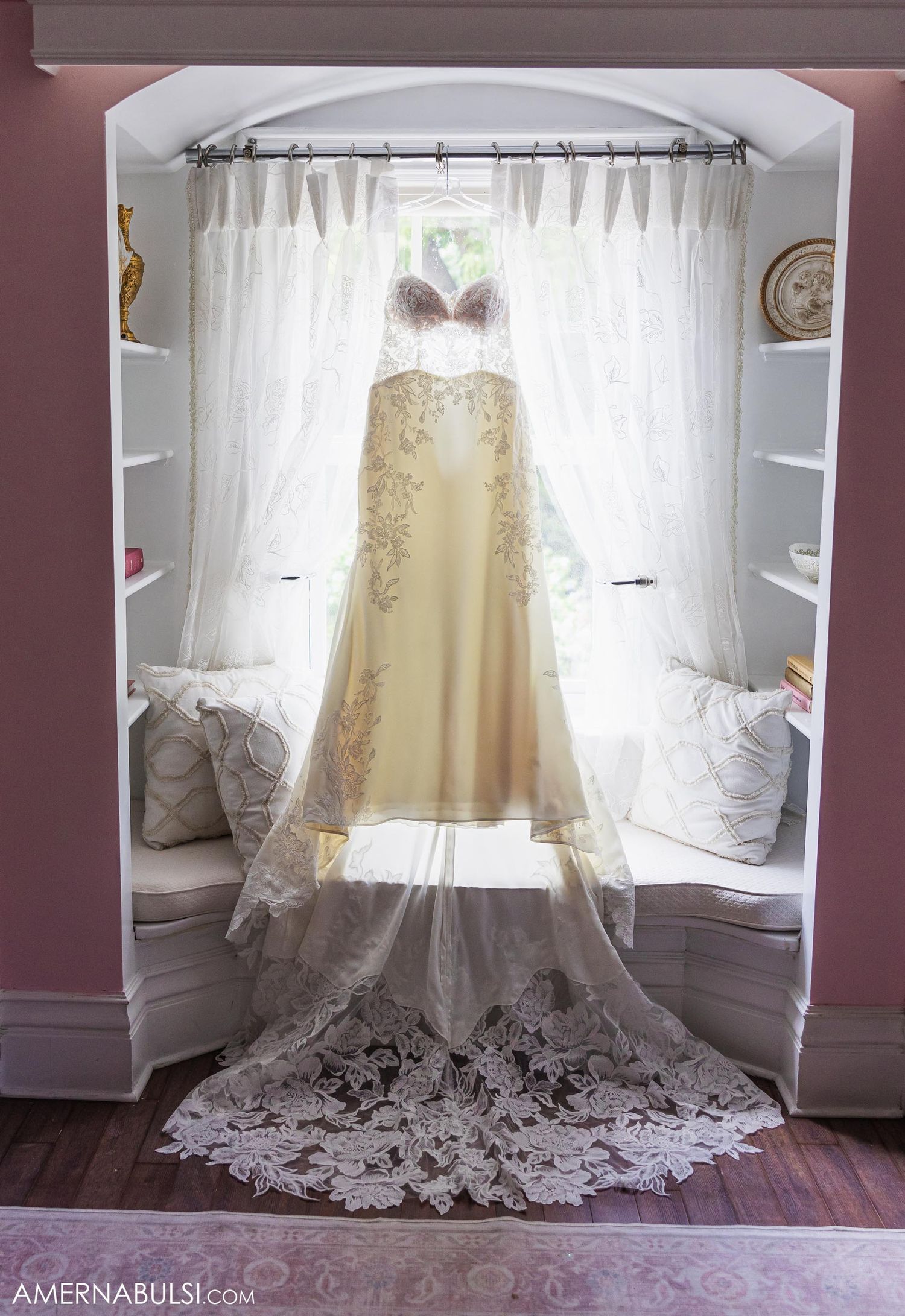Elegant champagne-colored wedding dress with lace train displayed between white curtains.
