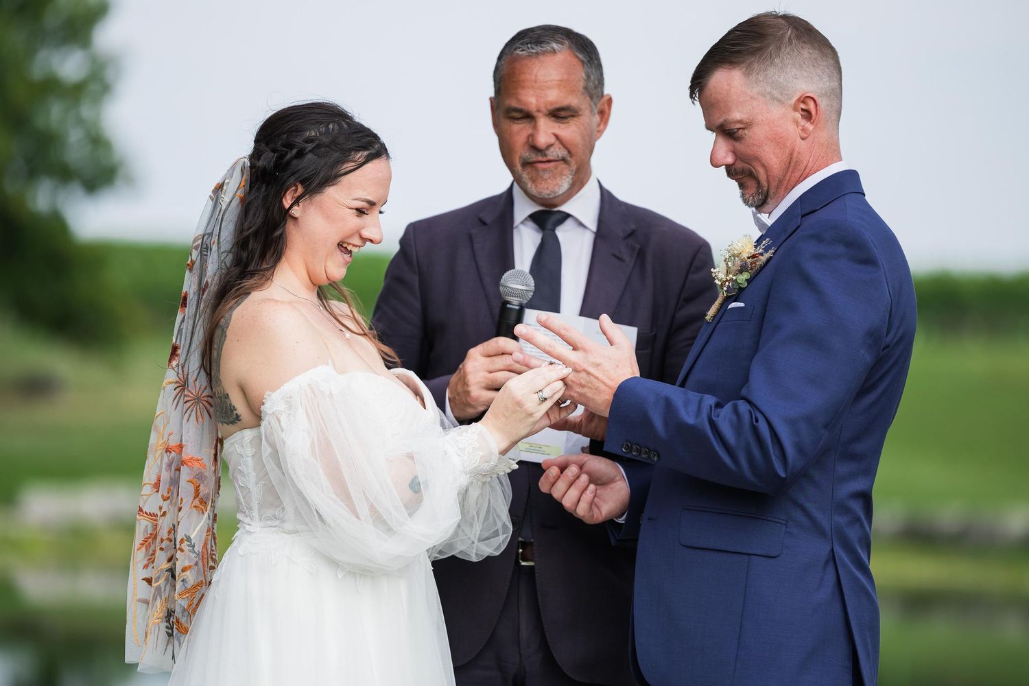 An intimate wedding ceremony moment unfolds at an outdoor venue with natural greenery in the background.