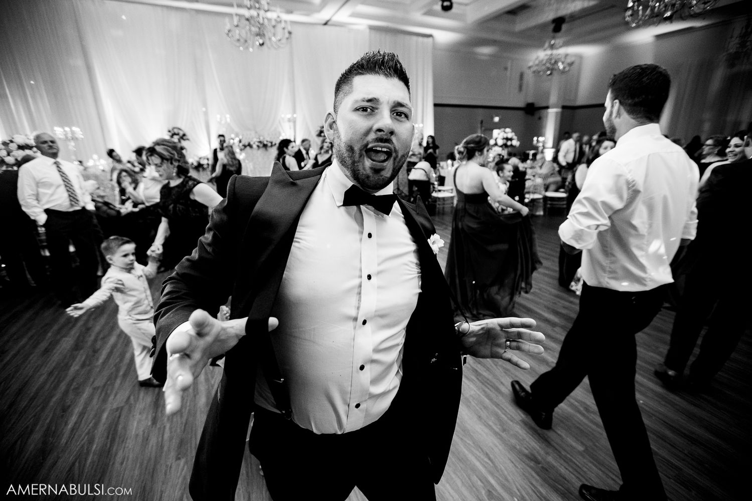 Wedding guests dancing together on a crowded reception dance floor during an evening celebration.