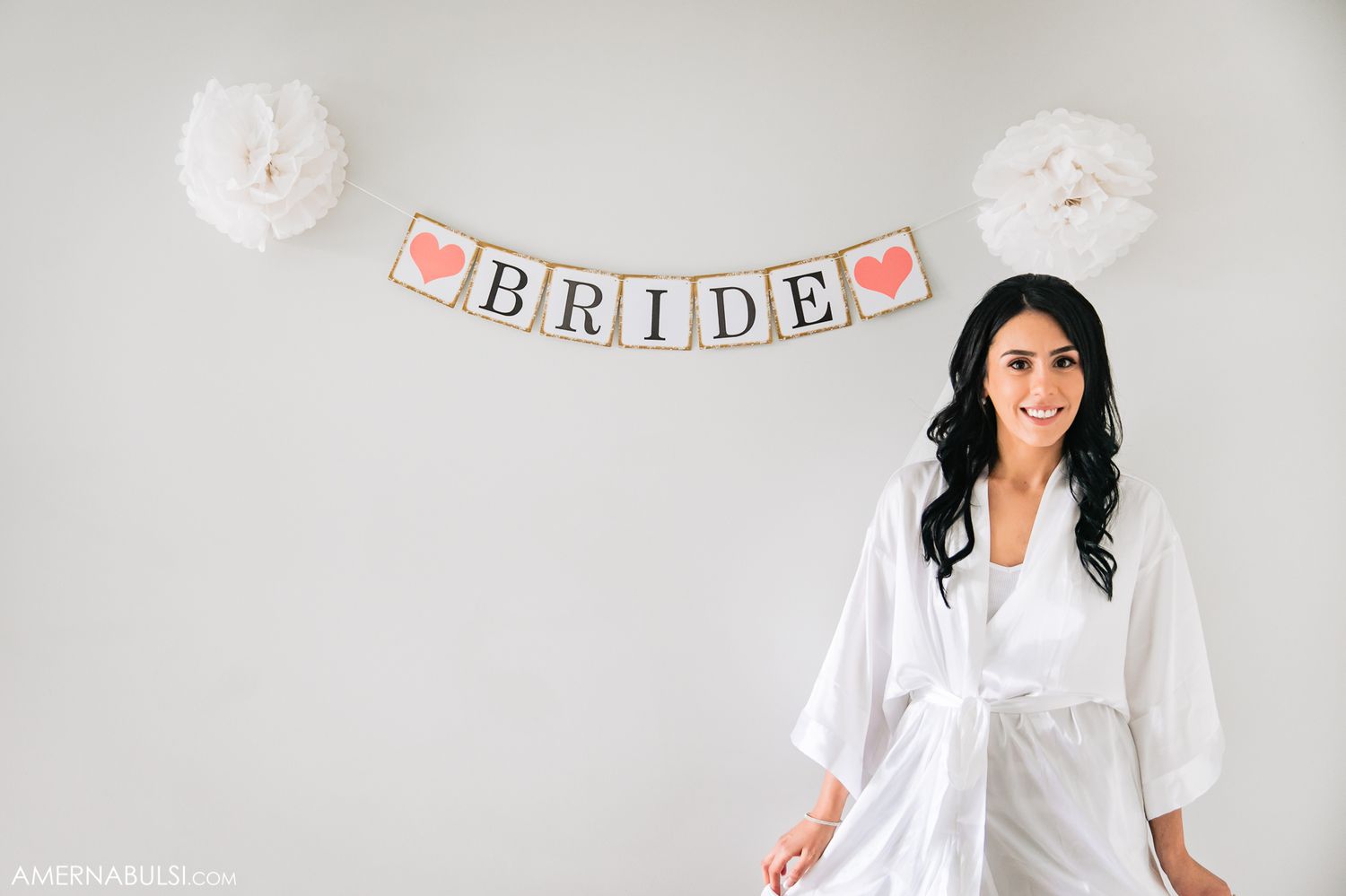 Group of women in white robes posing together for a bridal party photo shoot in a bright setting.