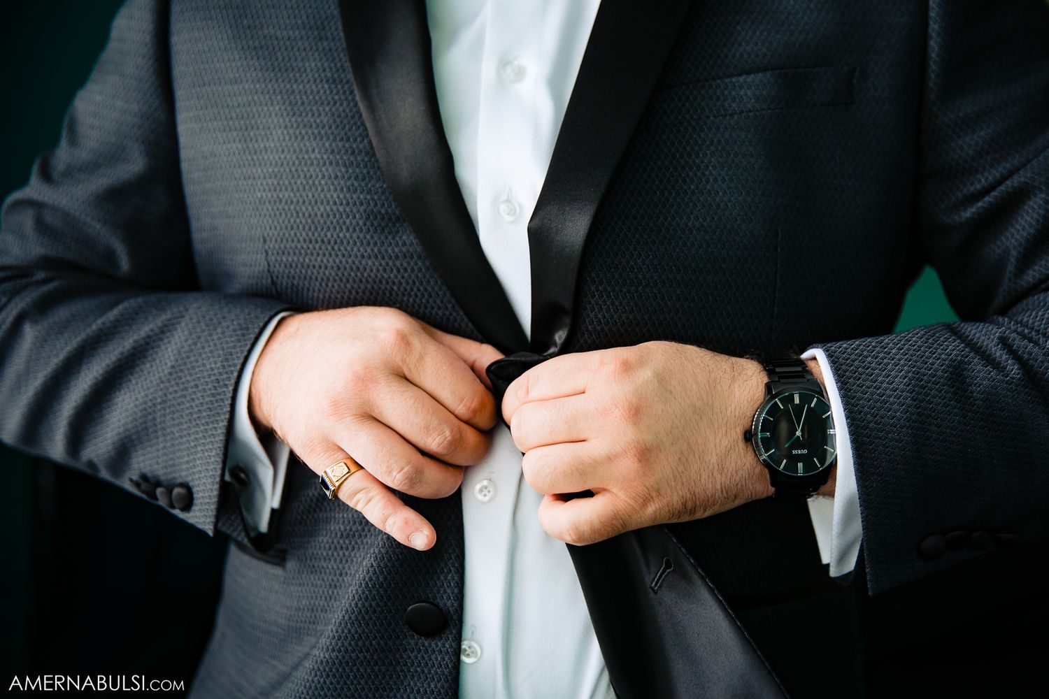 Close-up of someone adjusting the buttons on a formal black suit jacket.