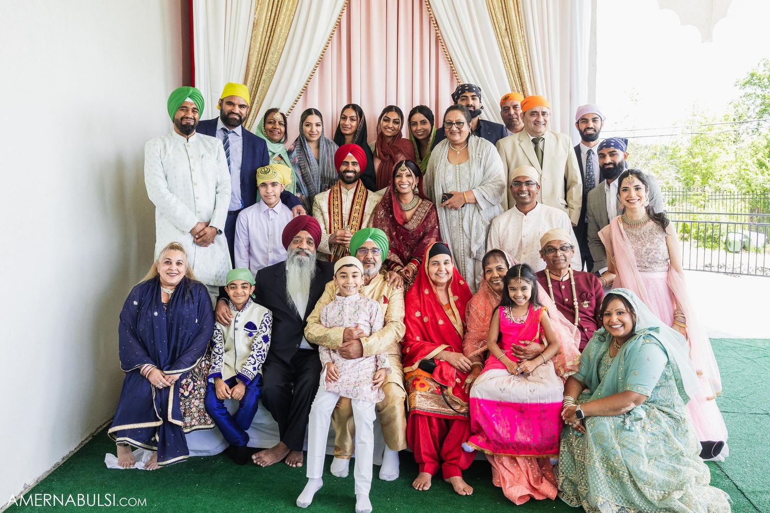 Large extended family group photo at Sikh wedding celebration with traditional outfits.
