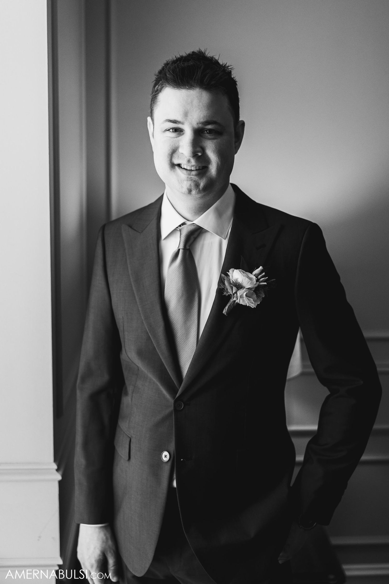 Black and white portrait of a groom in a classic suit with boutonniere smiling at camera.