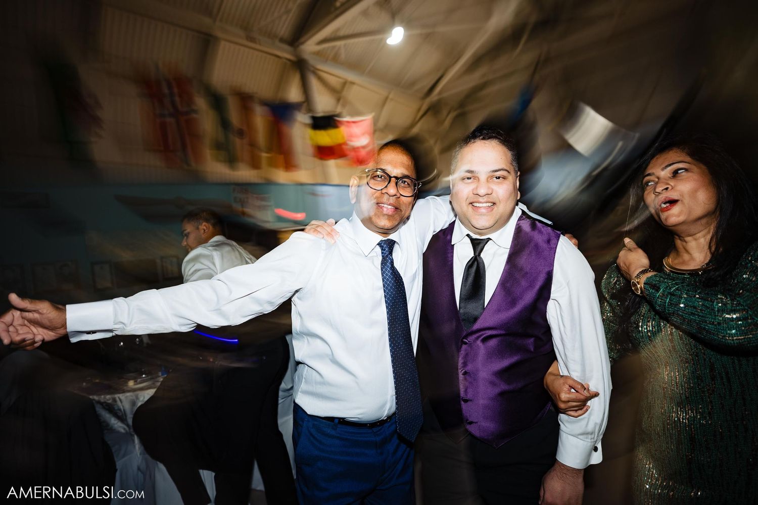 Wedding guests celebrating with arms spread wide during reception party.