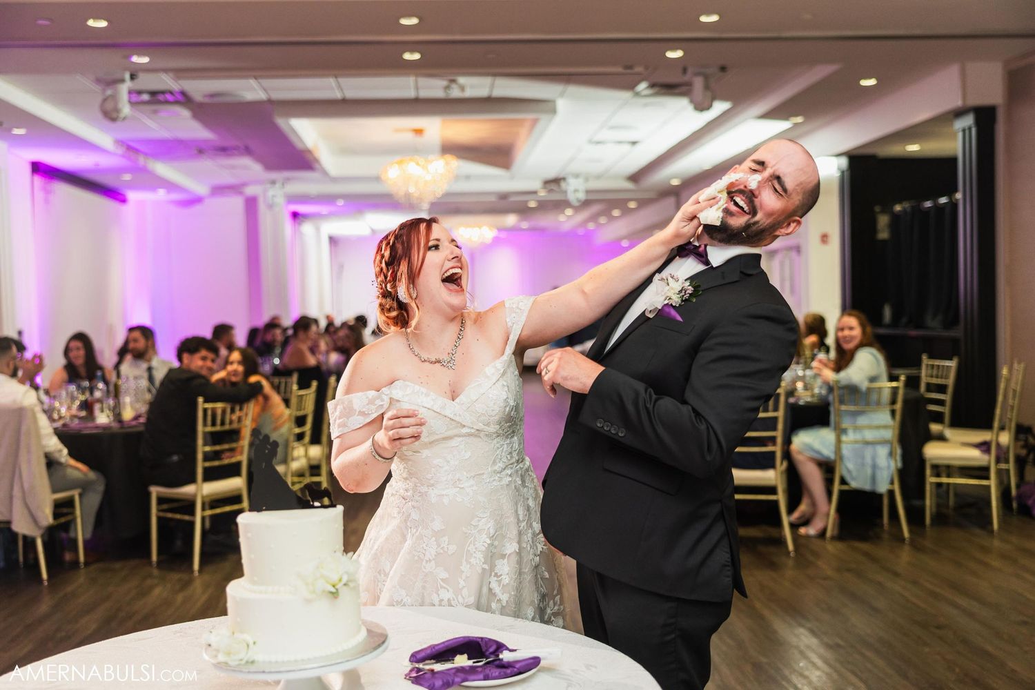 Couple having fun smearing cake on each other's faces during wedding reception.