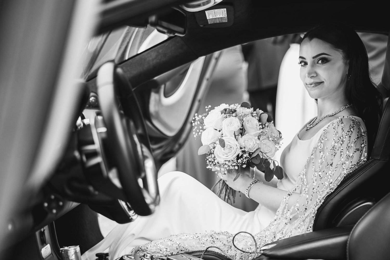 Black and white portrait of bride holding bouquet in car.