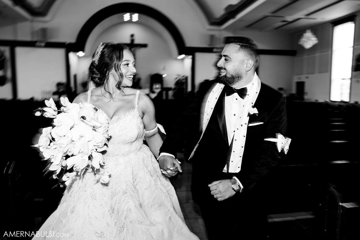 A joyful black and white photo of newlyweds sharing a candid moment in a church setting.
