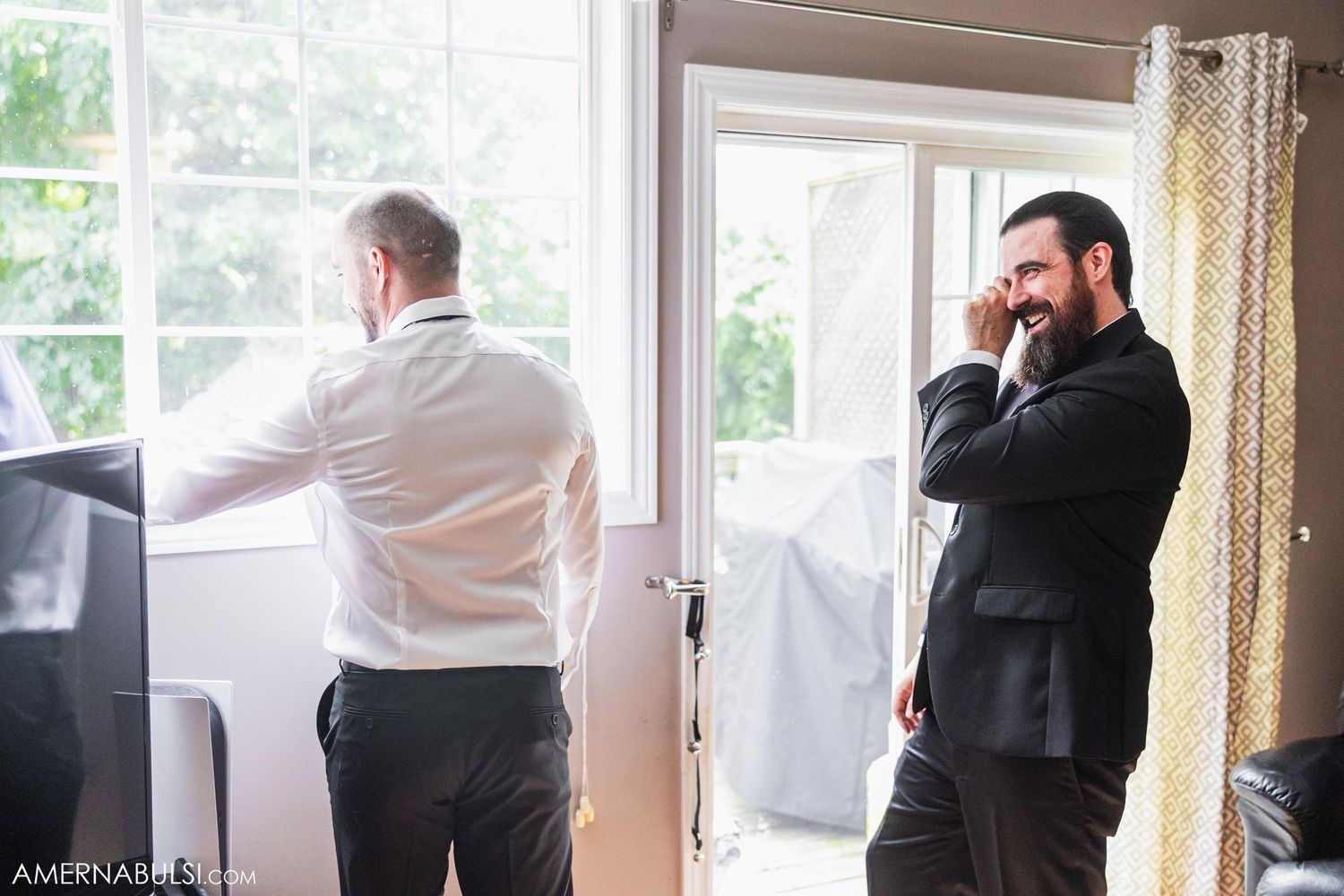 Two people in formal attire share a joyful moment in a bright room with windows.