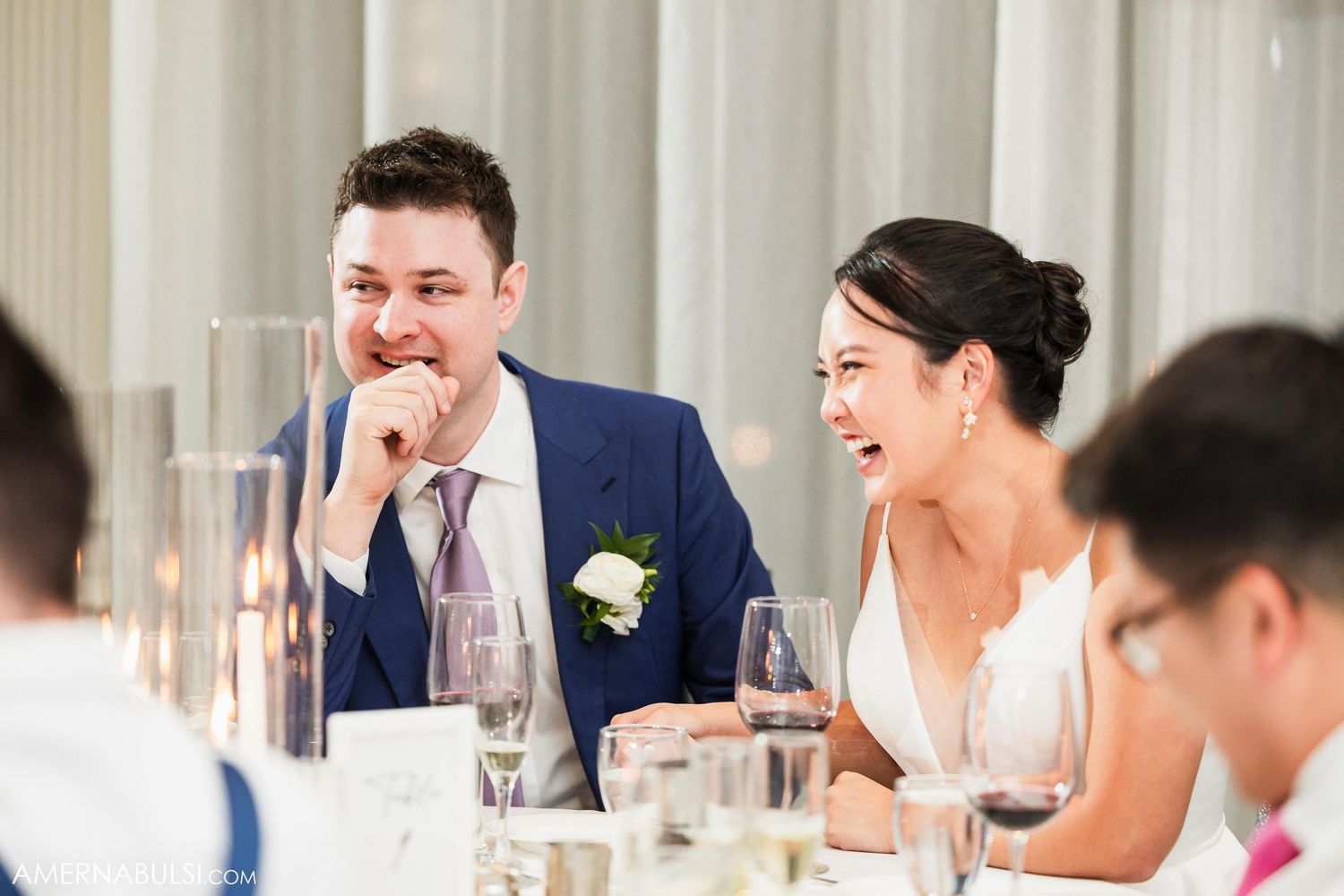 Candid moment of laughter between newlyweds during wedding reception dinner.