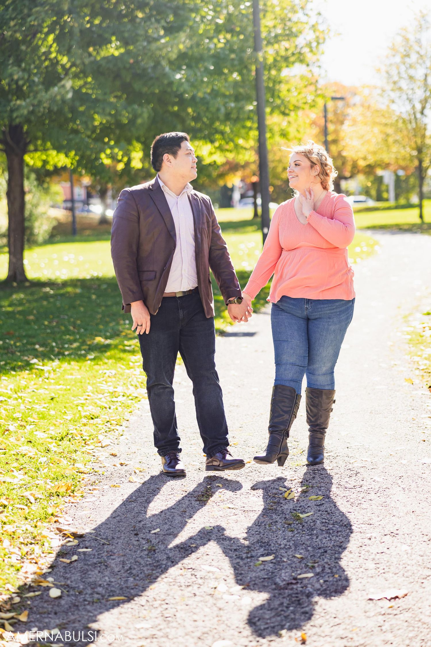 Couple walking hand in hand on a sunny autumn path with long shadows cast behind them on the trail.