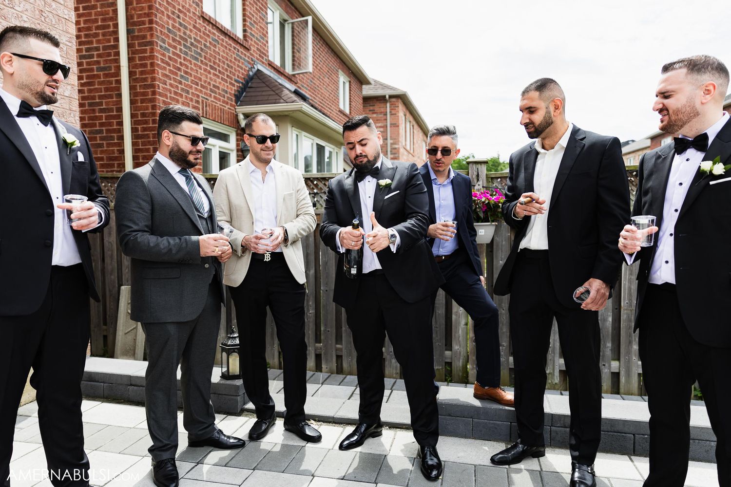 Group of formally dressed men in tuxedos checking their phones during wedding preparations.
