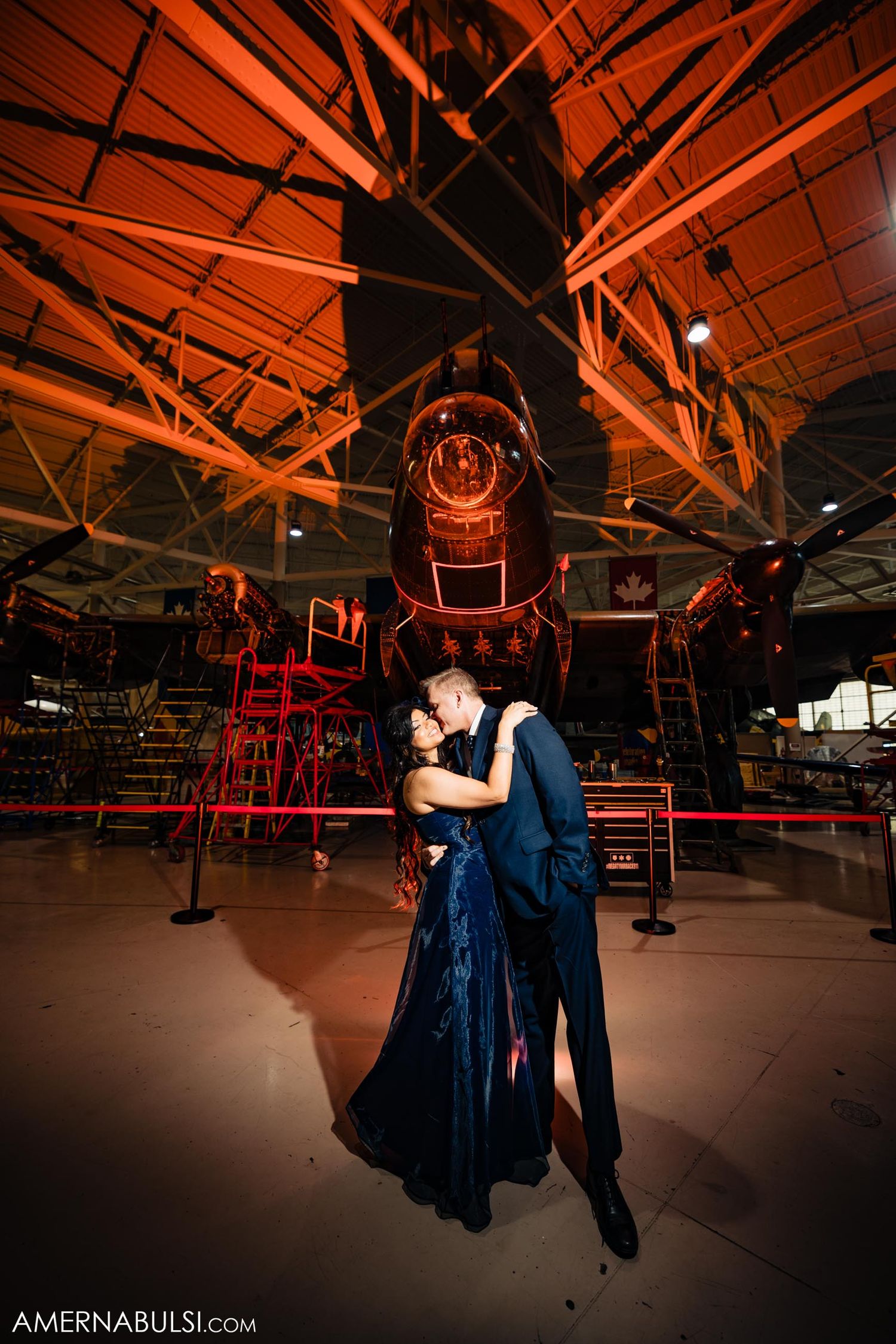 A couple shares an intimate dance under dramatic red lighting in an aviation museum.