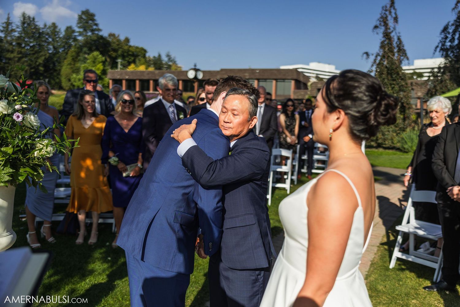 Joyful celebration at an outdoor wedding ceremony with guests seated on white chairs under blue skies.