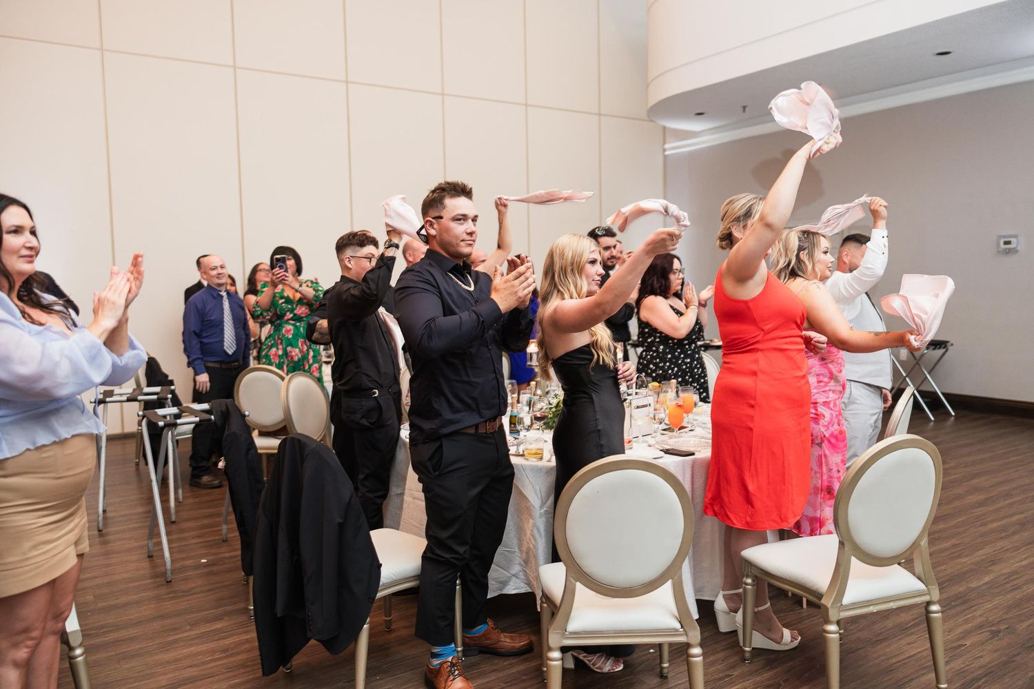 Wedding guests celebrating and dancing at reception with elegant white chairs.