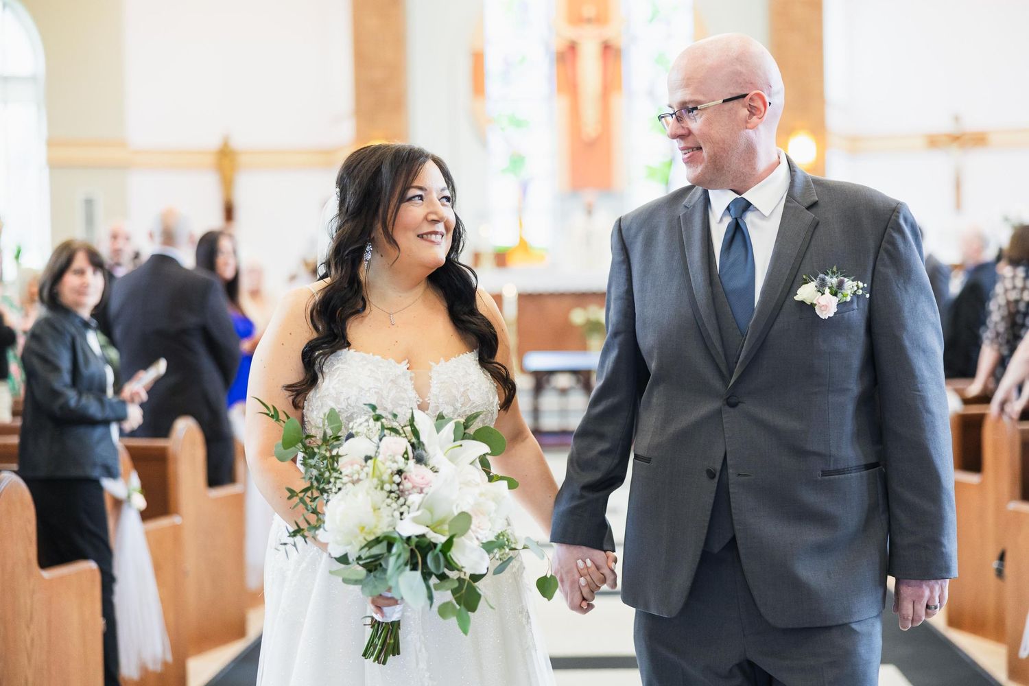 Elegant couple shares special moment in bright church interior with floral bouquet.