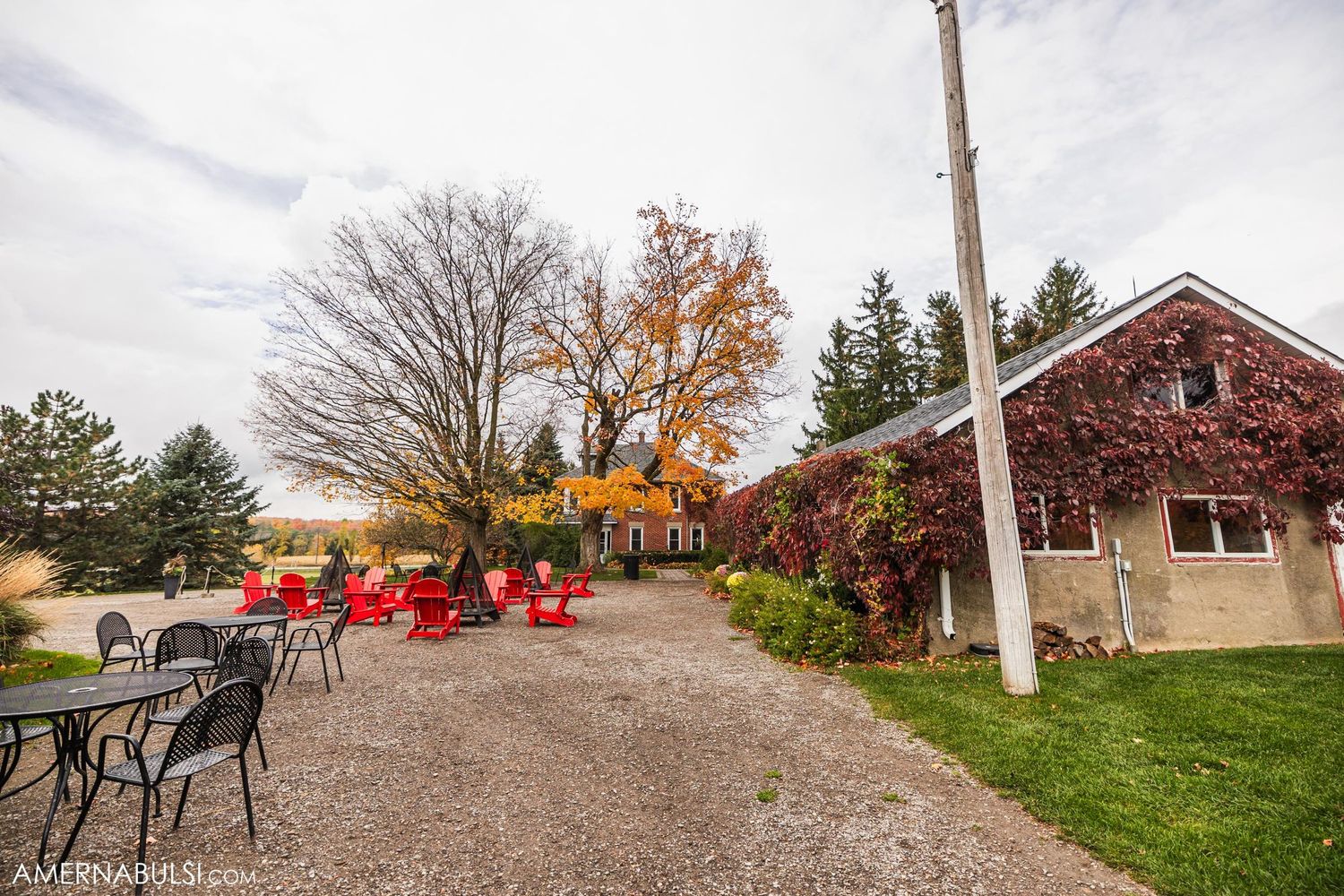 Rustic farm venue with red chairs and fall foliage on a cloudy day.