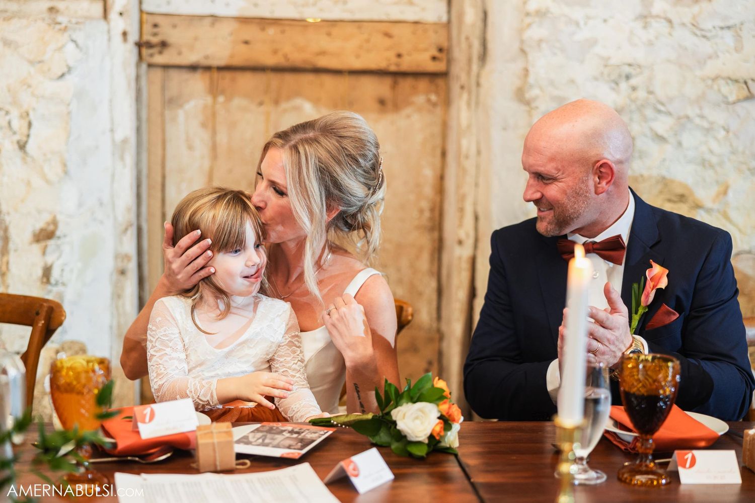 Family shares intimate moment at rustic wedding reception while dining at decorated head table.