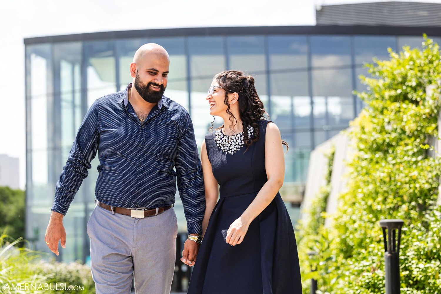 A couple walking together through a landscaped path near a modern building.
