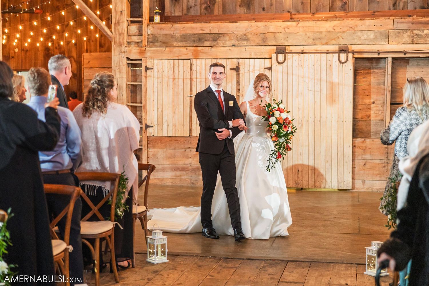 Rustic barn wedding ceremony with string lights, wooden details and floral arrangements.