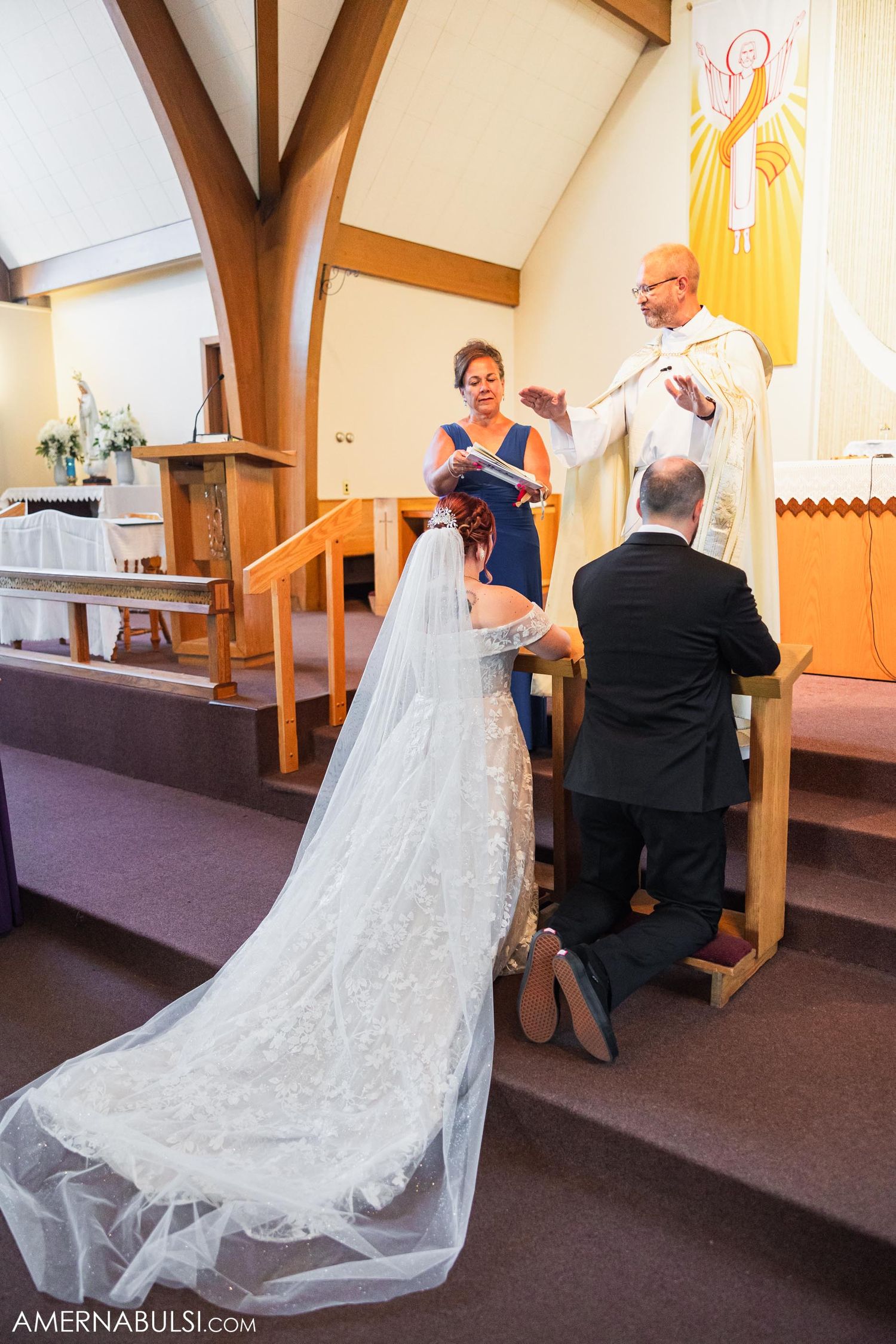 A white wedding dress with long train flows down church altar steps during the ceremony.