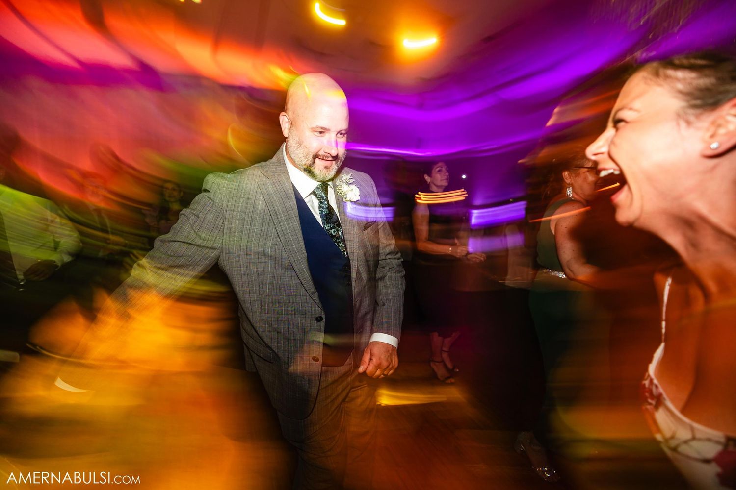 Dynamic motion blur capture of guests dancing at a wedding reception with colorful lighting.