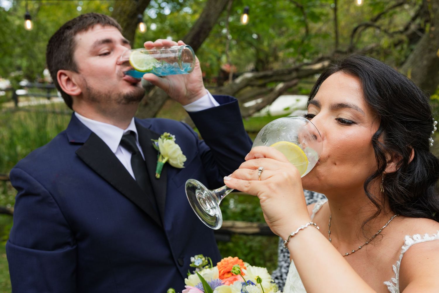 Bride and groom drink champagne together outdoors in a garden wedding celebration.