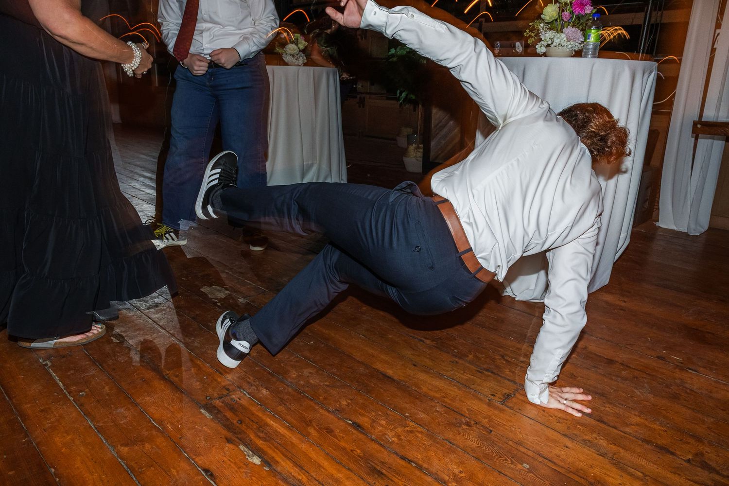 A guest breakdances on the wooden dance floor at a wedding reception venue.