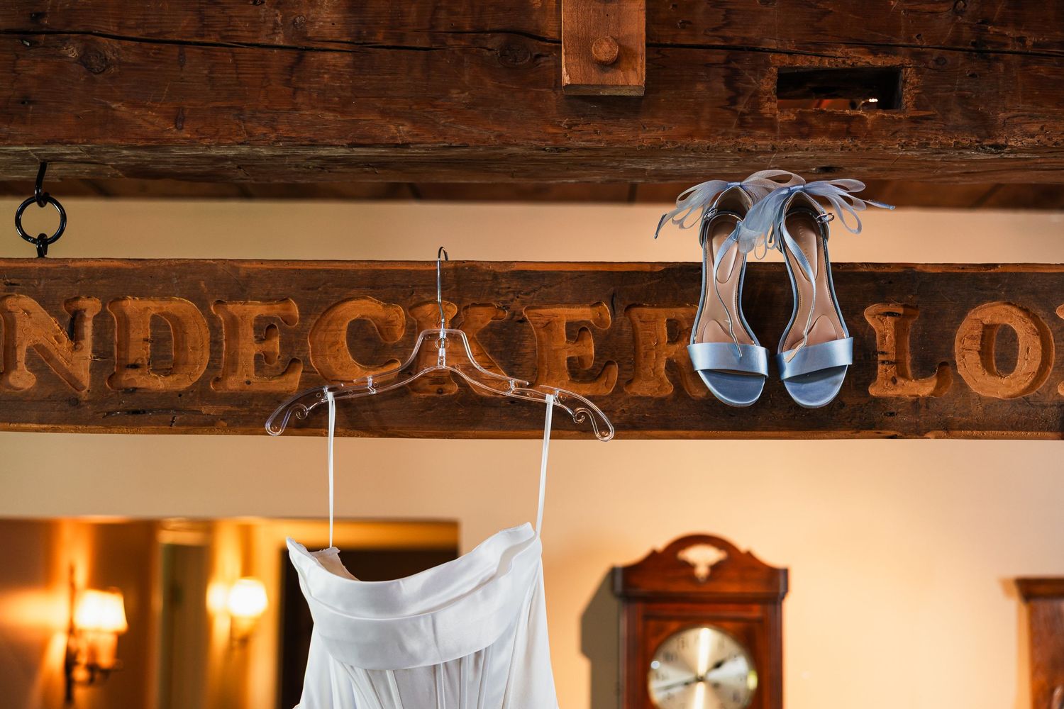 White wedding dress and blue heels hanging in front of a wooden Windecker Lodge sign indoors.