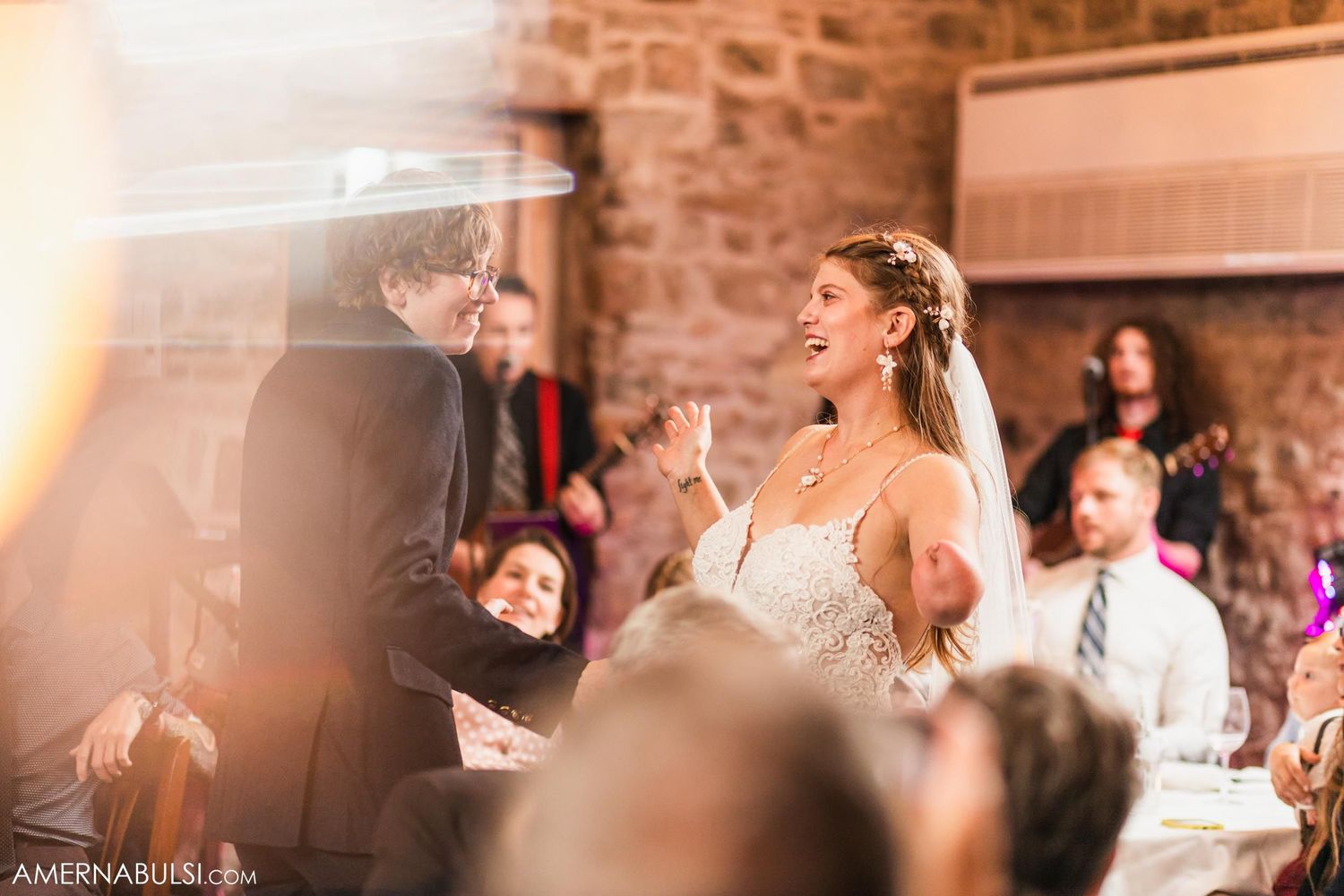 Candid moment during wedding speeches in stone-walled reception venue with natural lighting.