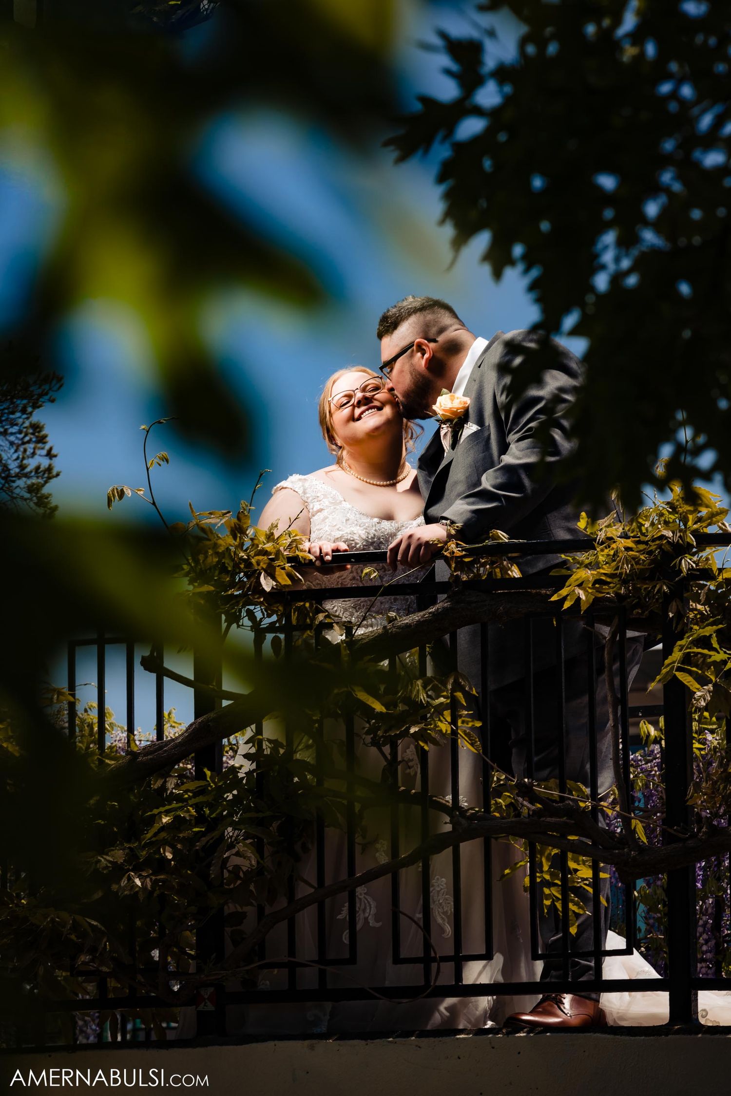 Romantic couple moment captured through foliage on an outdoor balcony.