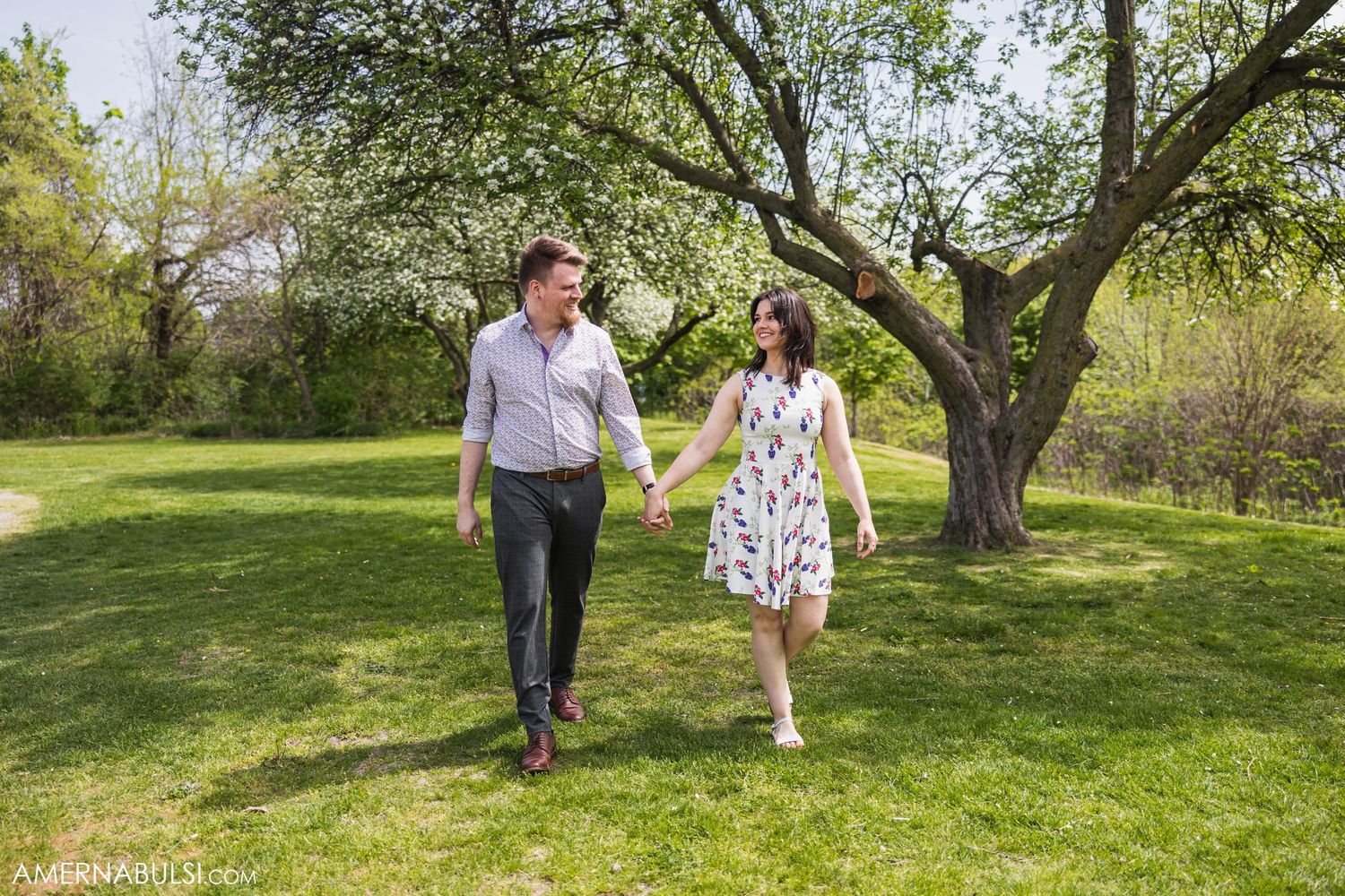 A couple takes a romantic stroll through a sunny spring garden holding hands.