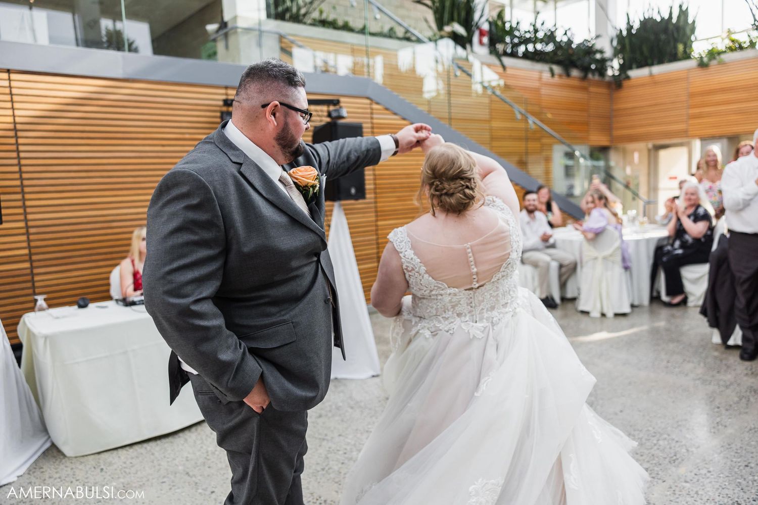 A couple shares a playful moment during their wedding dance in a light-filled venue.