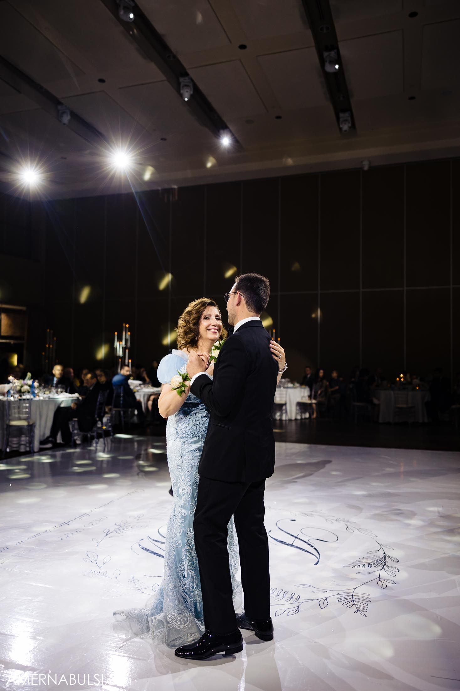 A couple dances together on an illuminated dance floor with twinkling lights and elegant decor.