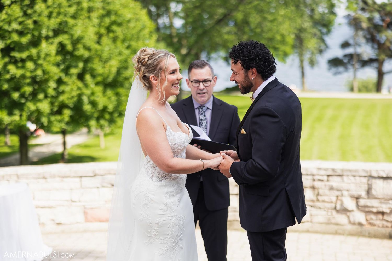 An outdoor wedding ceremony taking place on a beautiful sunny day with lush greenery in the background.