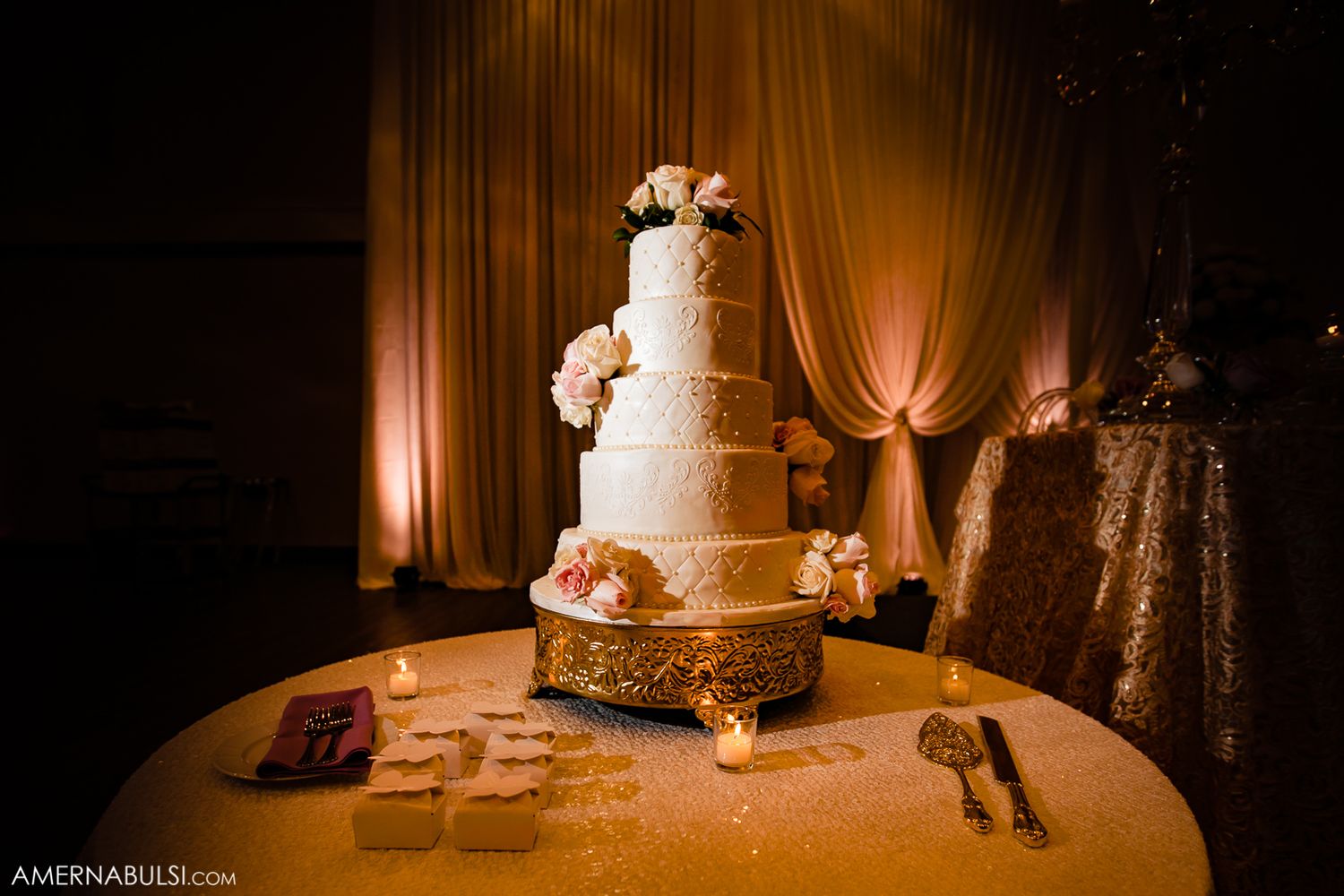 Romantic wedding reception venue with elegant amber lighting and white tiered cake on display.