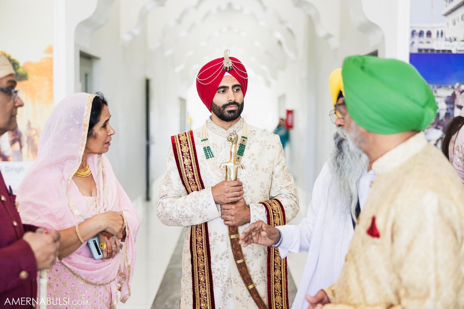 A groom in traditional Sikh wedding attire stands with ceremonial items during the celebration.
