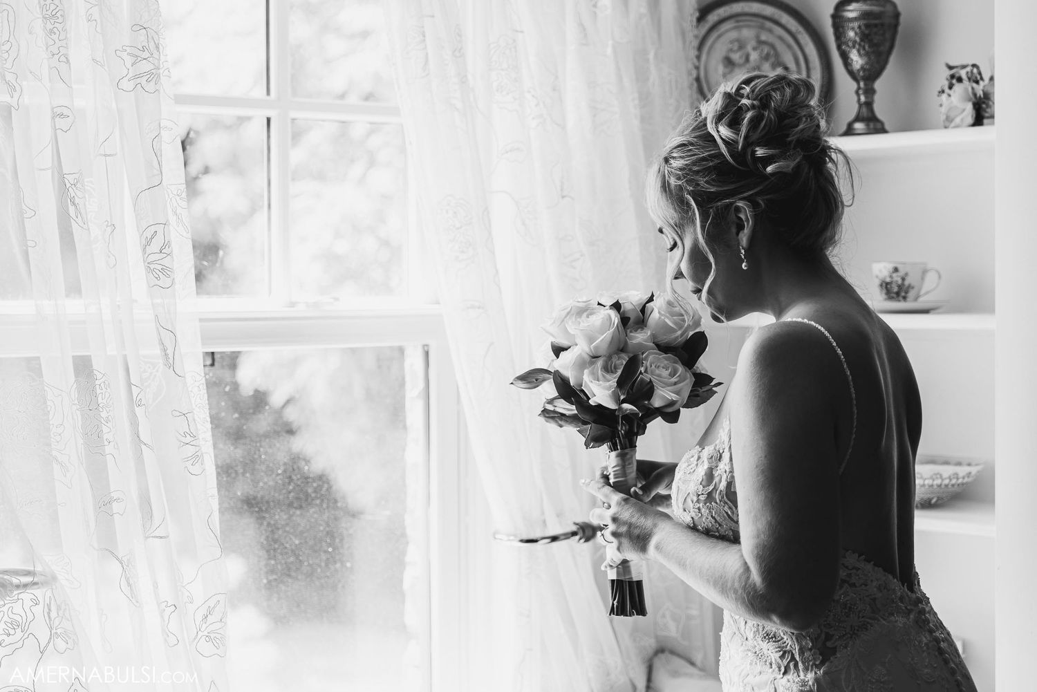 Black and white bridal portrait with bouquet silhouetted against window light.