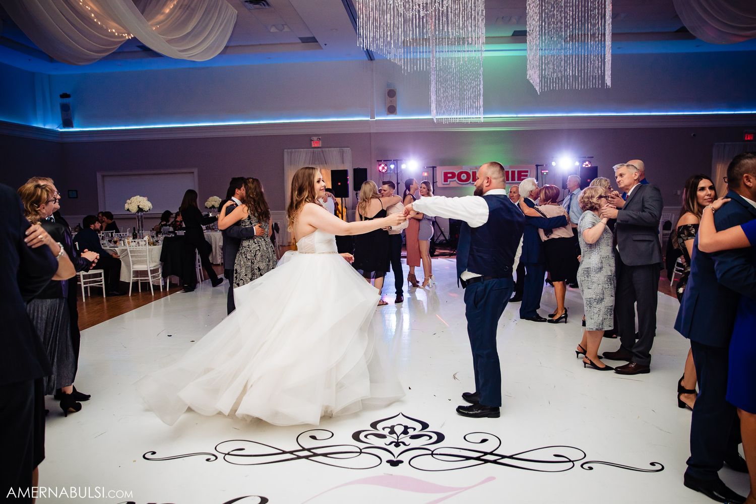 Couples dancing at a wedding reception with colorful lighting and a spacious dance floor.