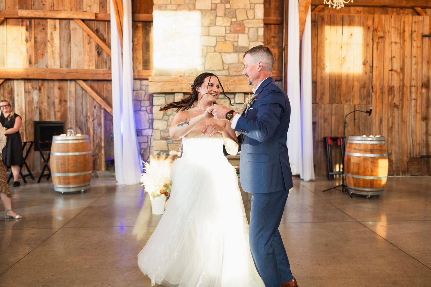 Couple shares an intimate dance moment in a rustic barn venue with decorative wine barrels.