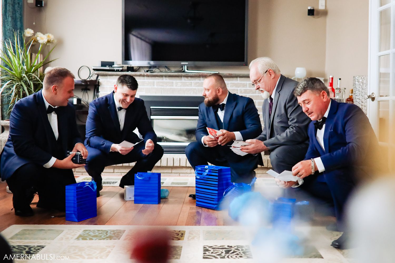 Groomsmen in blue suits sit together opening matching gift boxes before the ceremony.