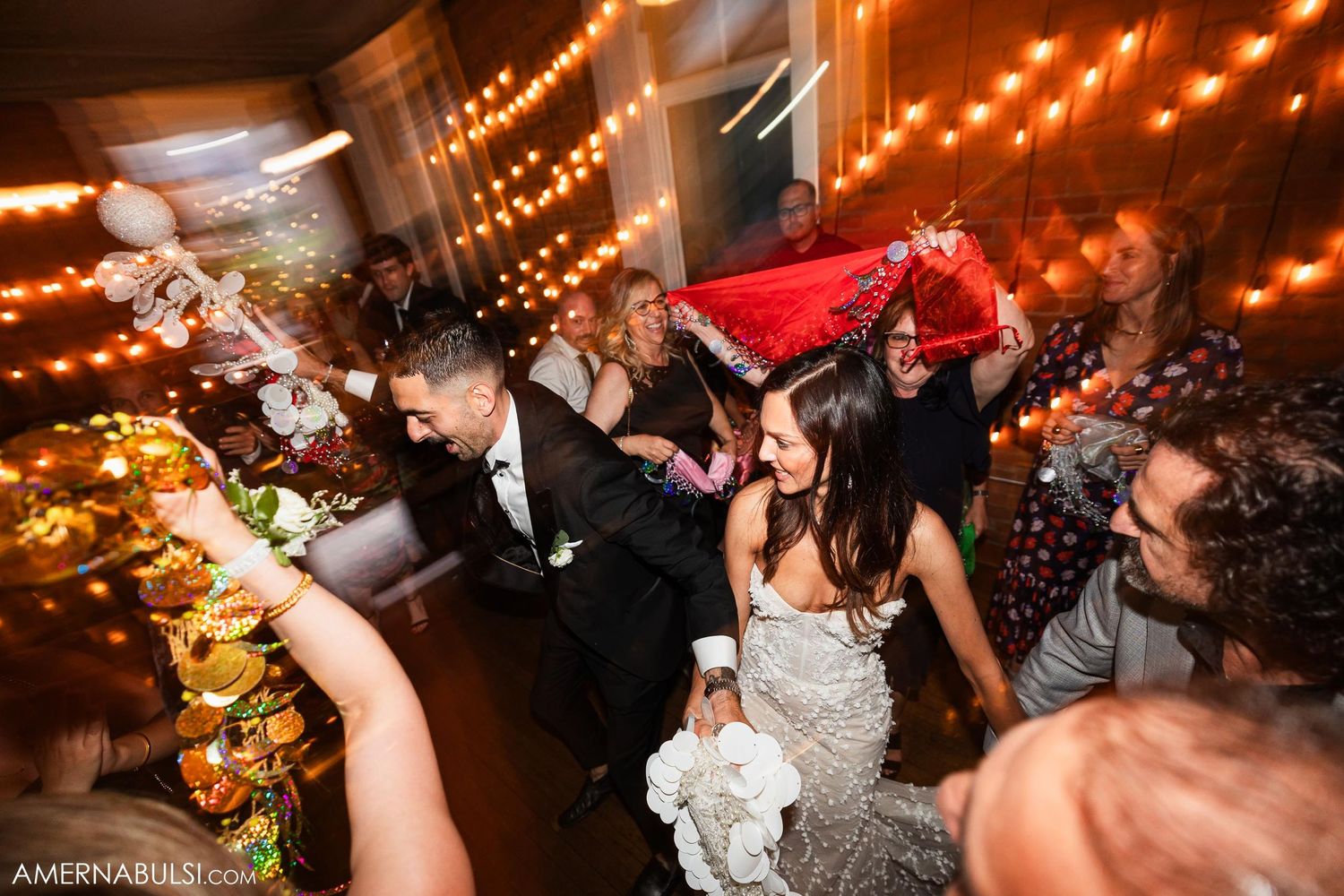 Lively wedding reception celebration with guests dancing under string lights.