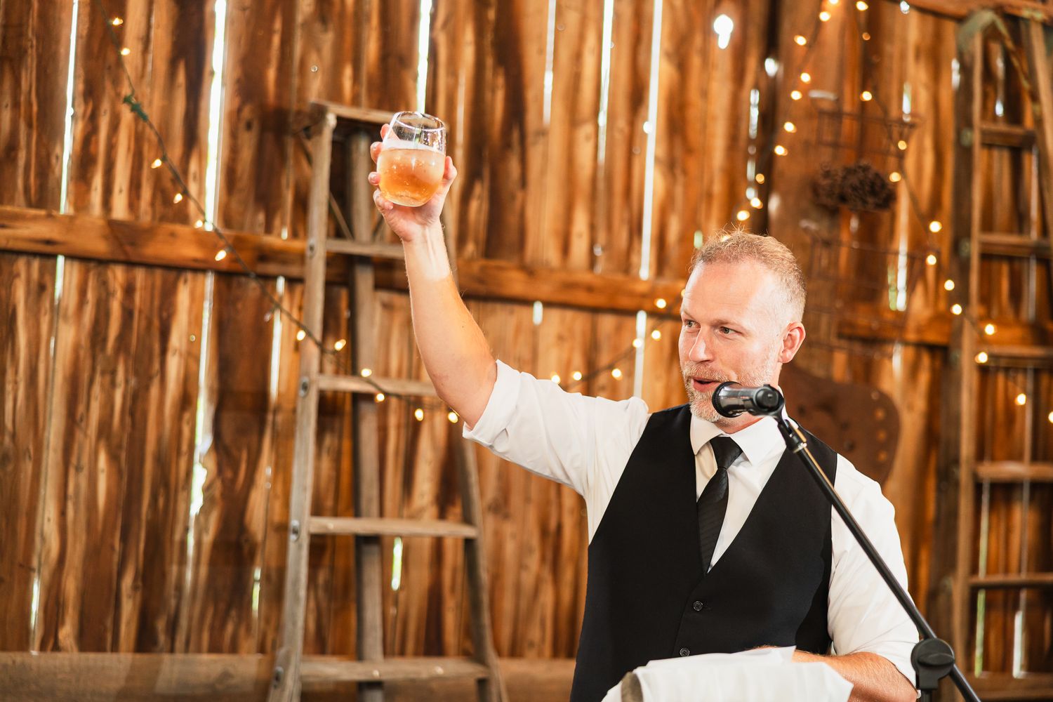 Wedding guests dance and celebrate inside a rustic wooden barn during a reception party.