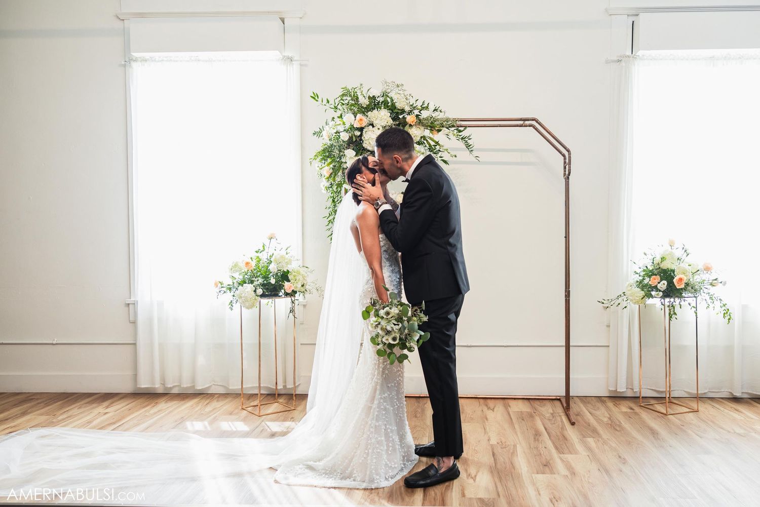 Wedding couple poses under a modern copper arch with floral arrangements.