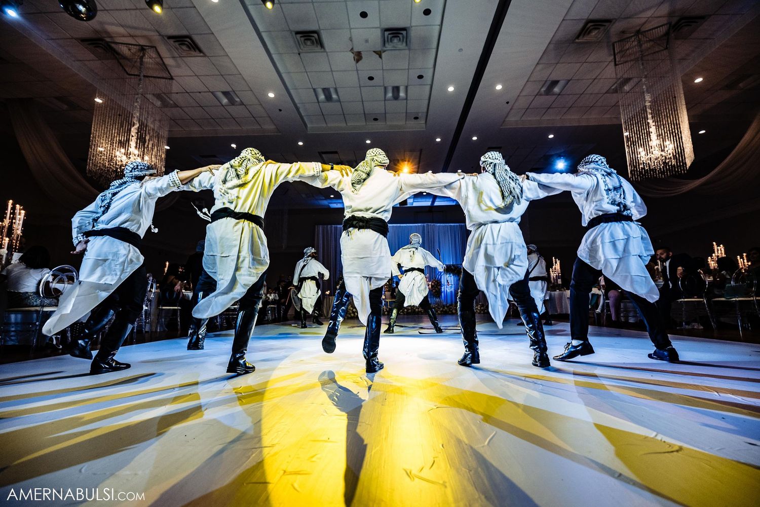 Traditional dancers in blue costumes perform synchronized leaps during an energetic folk dance performance.