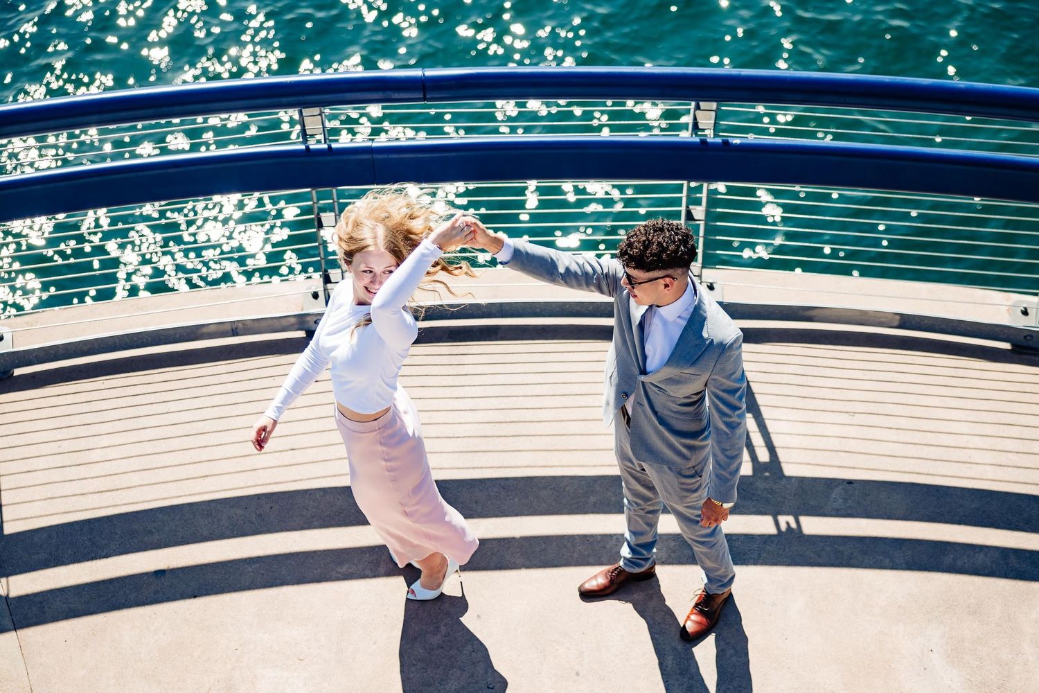 Couple dancing playfully on boat deck with turquoise ocean waters below.