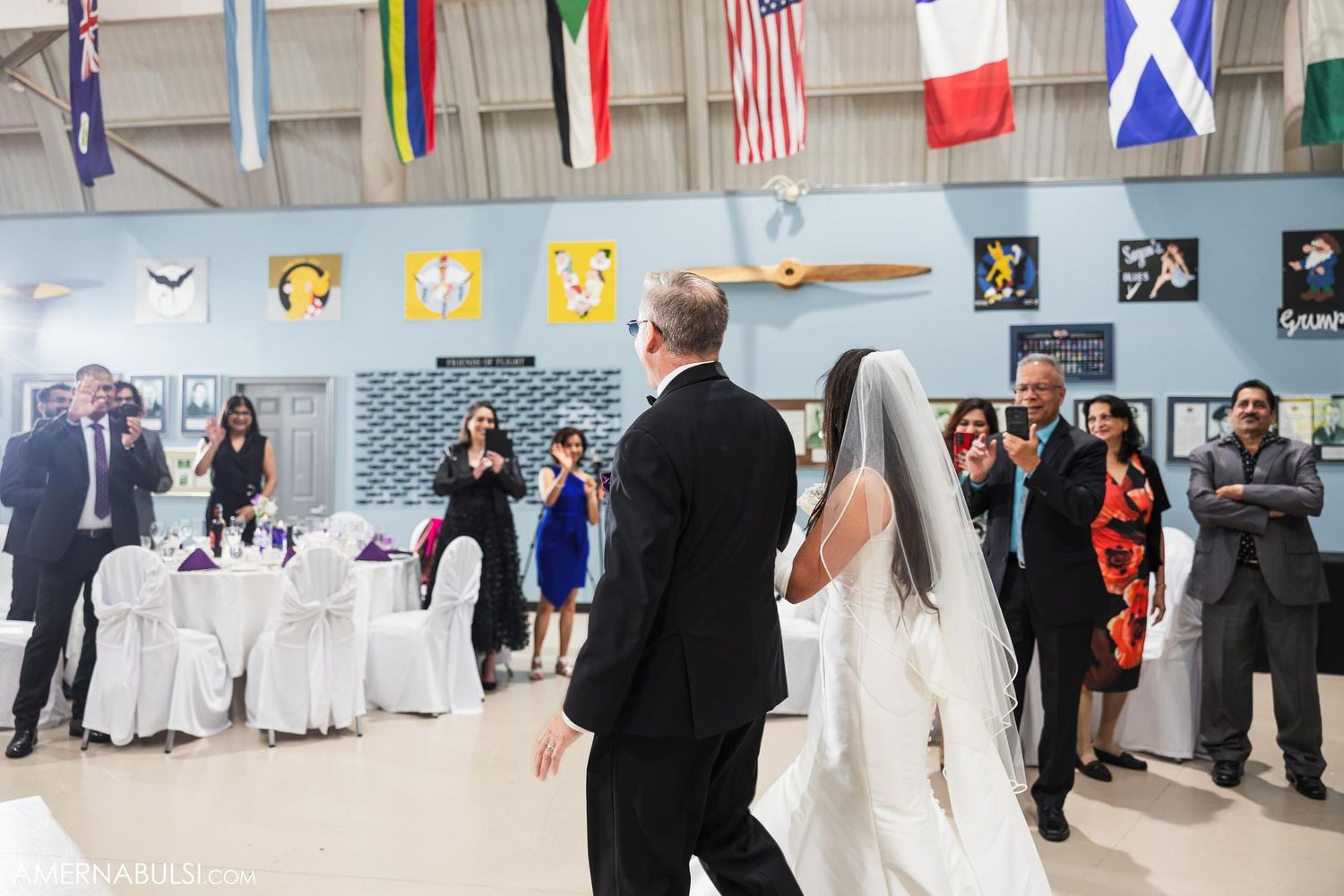 Wedding celebration with dancing and festivities in aviation museum with flags overhead.