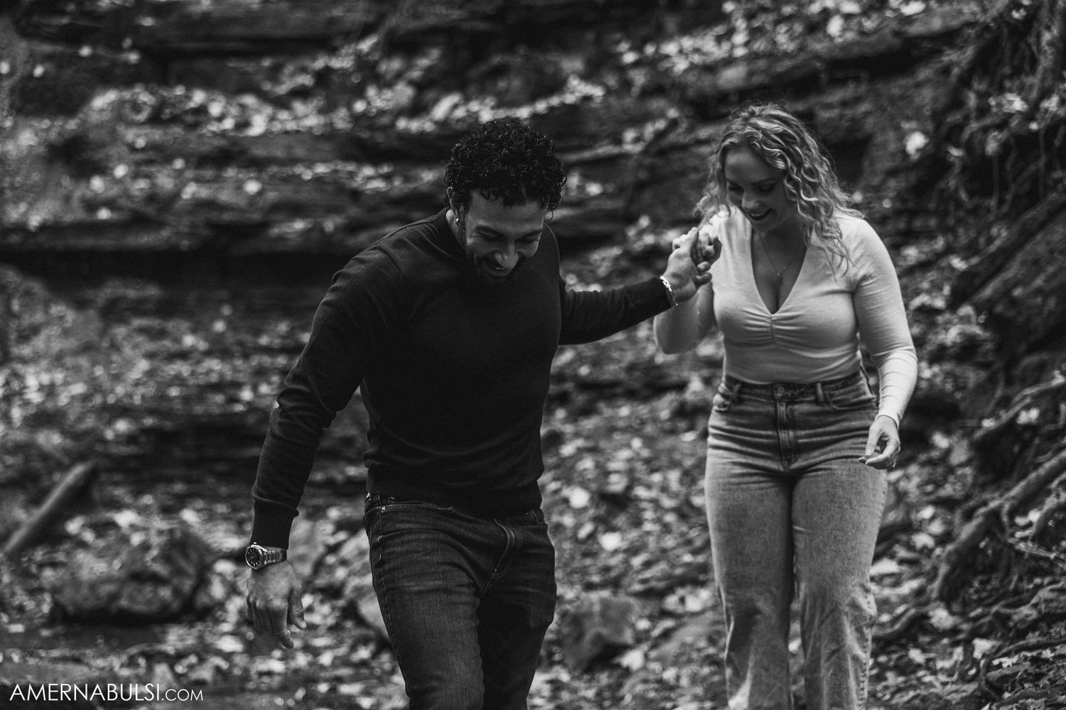 A couple helps each other traverse rocky terrain during their forest adventure.